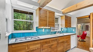 Une cuisine moderne avec des meubles en bois, une cuisinière à gaz et une vue sur l’extérieur par une fenêtre.
