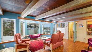 Un salon spacieux avec des poutres en bois, de grandes fenêtres et un tapis rouge.