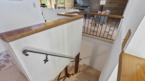 A staircase with a wooden handrail and metal balusters, leading to a landing with a white wall and a wooden railing.