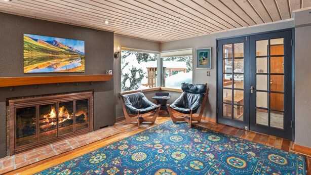 A cozy room with a fireplace, two leather chairs, a patterned rug, and a large window. - Historic, Heart of City Home - Near U/Med District (Anchorage)