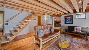 A spacious living area with a wooden staircase, leather sofa, and a glass coffee table. - Historic, Heart of City Home - Near U/Med District (Anchorage)