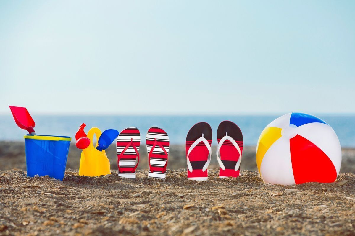 A beach scene with a blue bucket, yellow shovel, striped flip-flops, red and white striped flip-flops, and a beach ball.