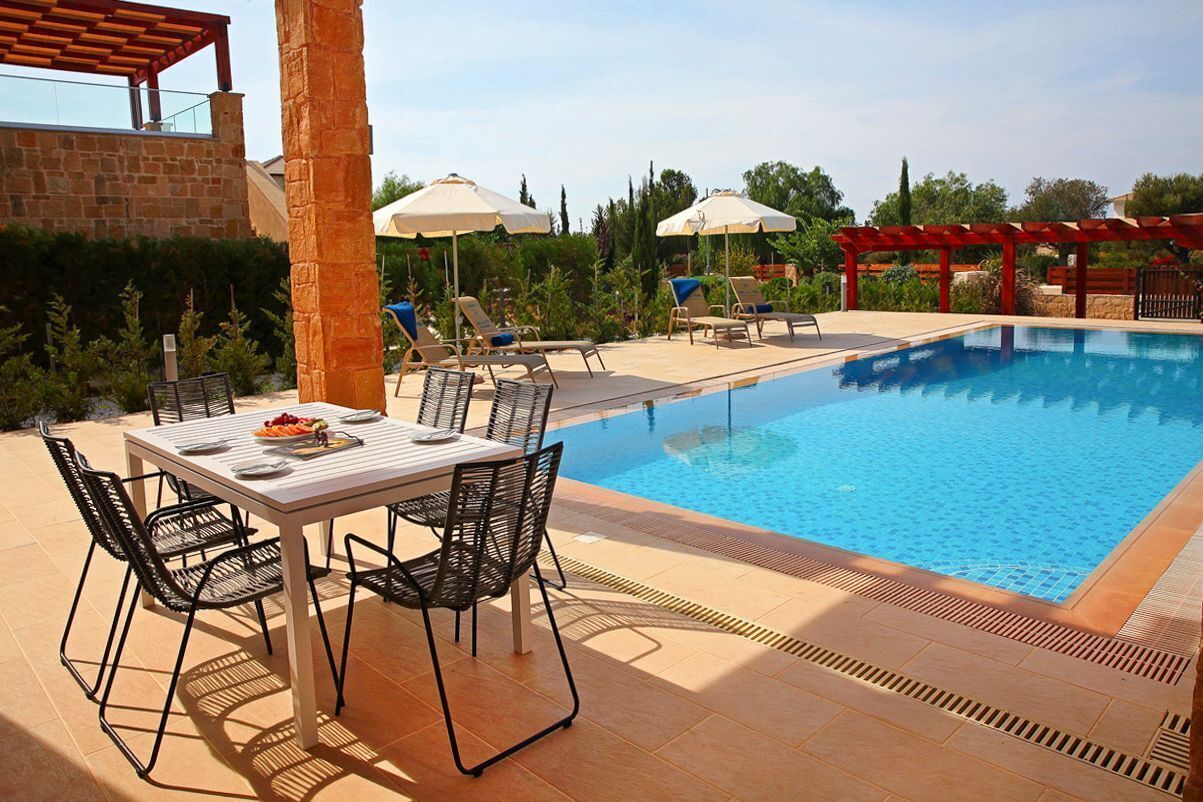 A poolside area with a table and chairs, umbrellas, and lounge chairs.