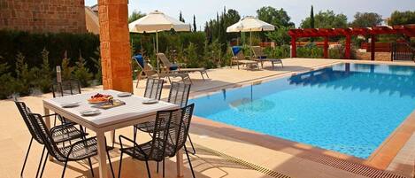 A poolside area with a table and chairs, umbrellas, and lounge chairs.