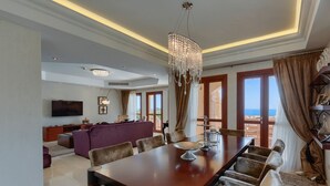 A spacious living area with a large wooden dining table, comfortable seating, a chandelier, and a television.