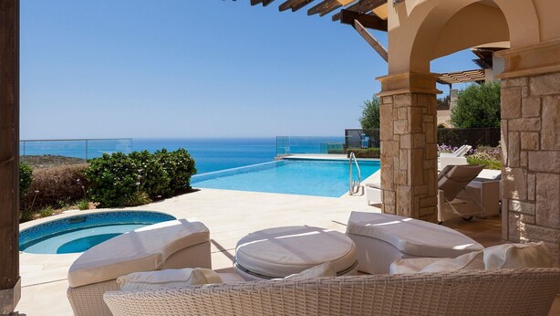 A pool area with a view of the sea, lounge chairs, and a pergola structure.