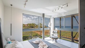 A modern bedroom with a large bed, a view of the sea, and a balcony with a chair.