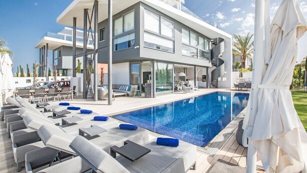 A modern hotel with a large outdoor pool, lounge chairs, and a two-story structure.