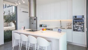 A modern kitchen with white cabinetry, a stainless steel range hood, a built-in oven, and a central island with bar stools.