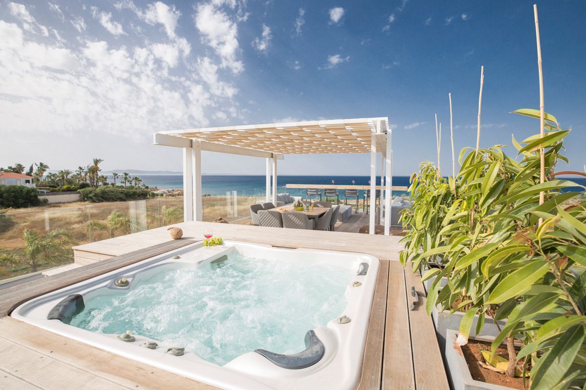 Un bain à remous avec une terrasse en bois, une pergola et une vue sur l’océan.