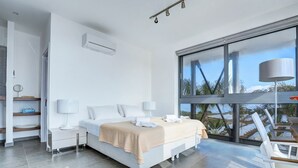 Ein modernes Schlafzimmer mit großem Fenster, einem Bett, Nachttischen und Blick ins Freie.