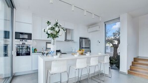 Eine moderne Küche mit weißen Schränken, Edelstahlgeräten, einer zentralen Kochinsel mit Barhocker und einem großen Fenster für natürliches Licht.