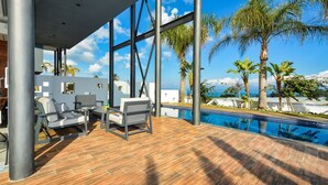 Ein moderner Poolbereich im Freien mit Holzterrasse, Liegestühlen und freiem Blick auf den Ozean.