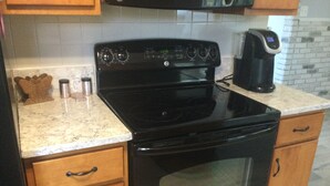 A kitchen with a black stove, wooden cabinets, and a marble countertop.