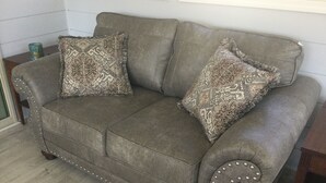 A gray upholstered sofa with decorative pillows and a beaded trim.
