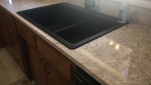 A kitchen with a black sink, a window, and a bottle of hand soap on the counter.