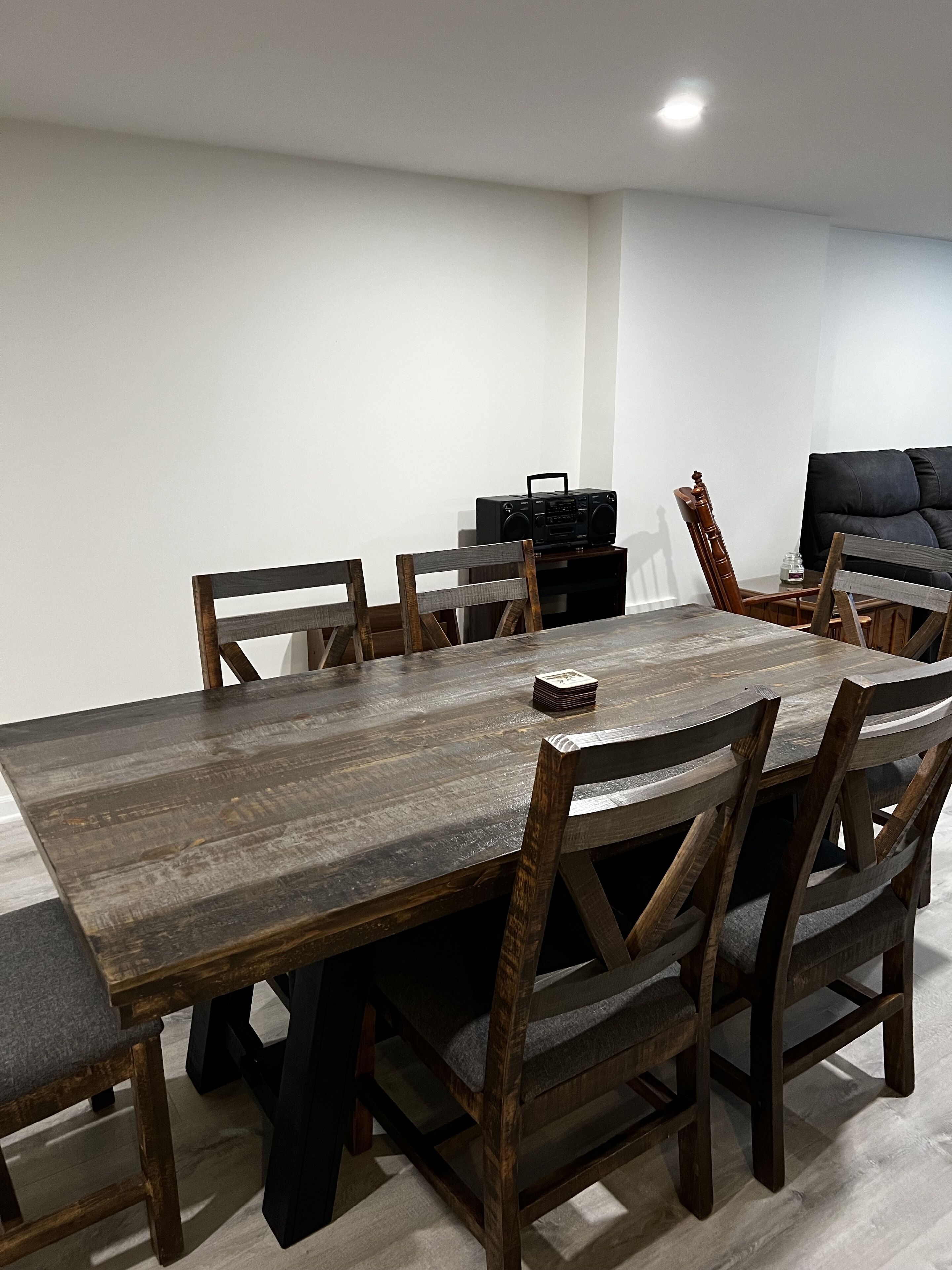 Un coin repas avec une table et des chaises en bois, une radio posée sur une table d’appoint et un canapé à l’arrière-plan.