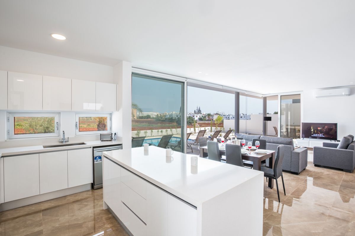 A modern kitchen with a large island, dining area with a view, and a living room with a flat-screen TV.