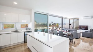 A modern kitchen with a large island, dining area with a view, and a living room with a flat-screen TV.