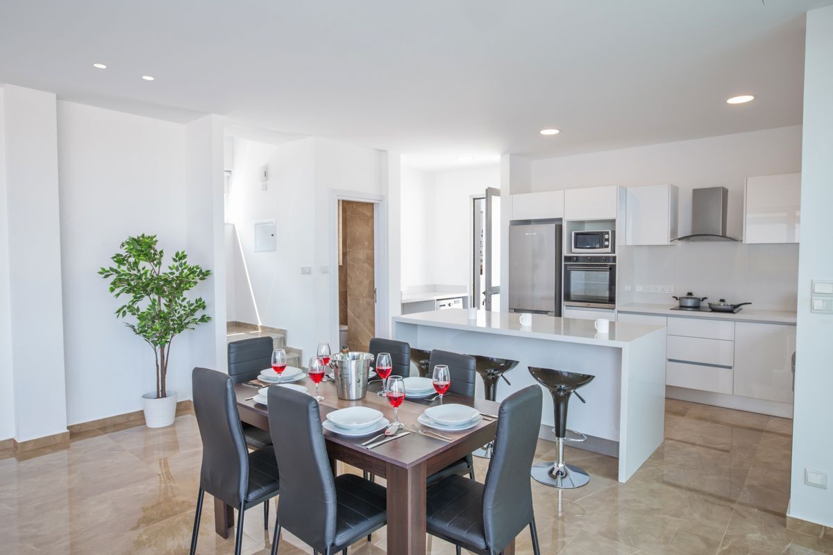 A modern kitchen with white cabinets, a central island, and a dining area with a table set for four.
