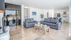 A spacious living area with two grey sofas, a wooden coffee table, and a large window offering a view of palm trees.