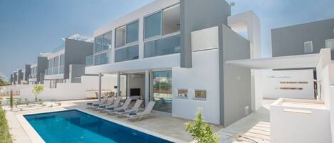 A modern hotel with a swimming pool, lounge chairs, and a clear view of the city skyline.