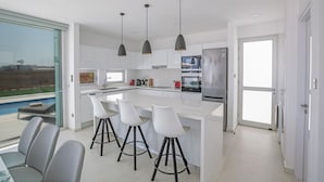 Een moderne keuken met een groot eiland, barstoelen, hanglampen en uitzicht op een zwembad.