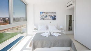 Een moderne hotelkamer met een groot bed, een schilderij aan de muur en uitzicht op een stadsgezicht door een groot raam.