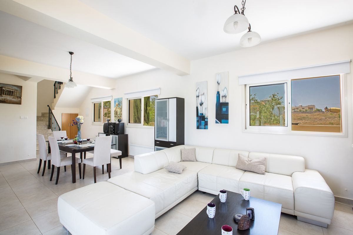 A modern living room with a white sofa, a dining table with chairs, and artwork on the walls.