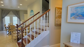 A staircase with wooden handrails and white balusters, leading to a dining area with a wooden table and chairs. - FREE Reserved Beach Chairs & Umbrellas ♥ Across from Beach ♥Bikes+Game Room+Pool (Destin)
