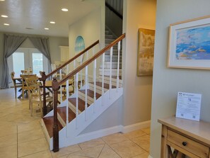 A staircase with wooden handrails and white balusters, leading to a dining area with a wooden table and chairs.