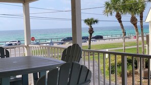 A balcony with a table and chairs overlooking a road with parked cars and a stop sign.