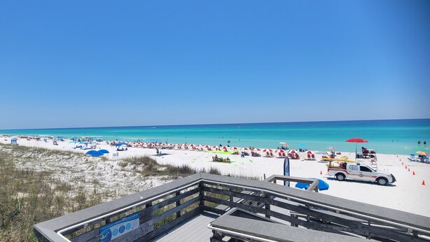 A beach with a wooden boardwalk, beach umbrellas, and a lifeguard tower.