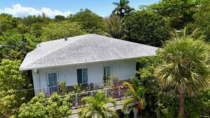 A white building with a grey roof, surrounded by lush greenery and a clear sky. - Your Grove Home (Miami)