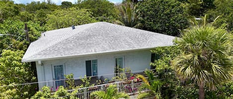 A white building with a grey roof, surrounded by lush greenery and a clear sky.