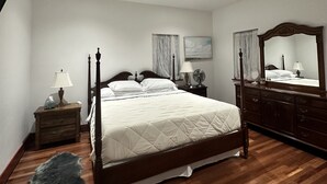 A bedroom with a four-poster bed, wooden nightstands, a dresser, and a large mirror. - Your Grove Home (Miami)