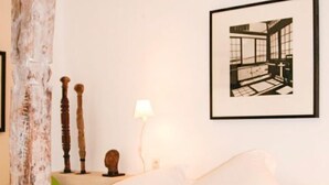 A bed with white linens and a colorful blanket, a framed picture on the wall, and a wooden pillar.