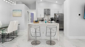 A modern kitchen with white cabinetry, a stainless steel refrigerator, and a marble countertop. - Welcome to our Modern Cape Escape with Heated Pool (Cape Coral)