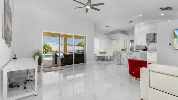 A modern, spacious living area with a white desk, a red chair, and a dining table. - Welcome to our Modern Cape Escape with Heated Pool (Cape Coral)