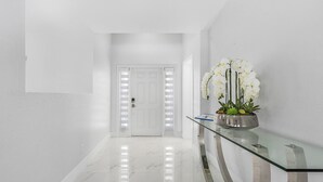 A modern hallway with a glass console table, a potted orchid, and a white door with illuminated panels. - Welcome to our Modern Cape Escape with Heated Pool (Cape Coral)