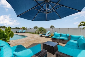 A backyard with a swimming pool, lounge chairs, and a large umbrella.