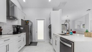 A modern kitchen with white cabinetry, stainless steel appliances, and a marble floor. - Welcome to our Modern Cape Escape with Heated Pool (Cape Coral)