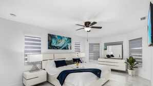 A modern bedroom with a large bed, bedside tables, a ceiling fan, and a large mirror. - Welcome to our Modern Cape Escape with Heated Pool (Cape Coral)
