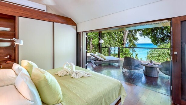 A bedroom with a bed, pillows, a green blanket, and a balcony with a view of the ocean. - Villa Lily Pad - Three Bedroom Villa, Sleeps 6 (Gibbes)