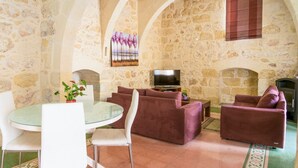 A stone-walled room with a fireplace, a television, and seating arrangements including a glass table and chairs.