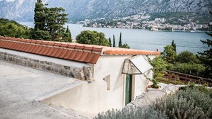 Un edificio costiero con tetto in tegole rosse, muro in pietra e vista su un lago e montagne sullo sfondo.