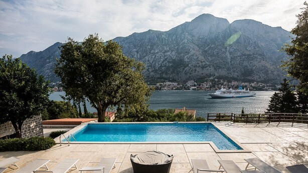 Piscina con lettini e vista su una montagna e una nave sullo sfondo.