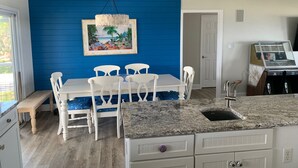 A kitchen with a granite countertop, white cabinets, and a dining area with a blue wall and white chairs. - Gulf to Bay, on the beach home with bay access (Alligator Point)