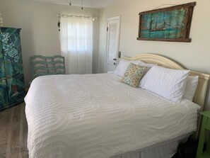 Ein Schlafzimmer mit einem großen Bett, einem hölzernen Kopfende, einem grünen Sessel, einem Kleiderschrank und einem Gemälde an der Wand.