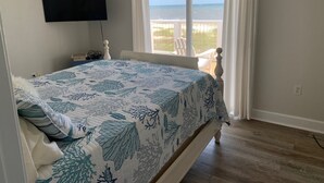 A bedroom with a bed, a TV mounted on the wall, a window with curtains, and a view of the ocean. - Gulf to Bay, on the beach home with bay access (Alligator Point)